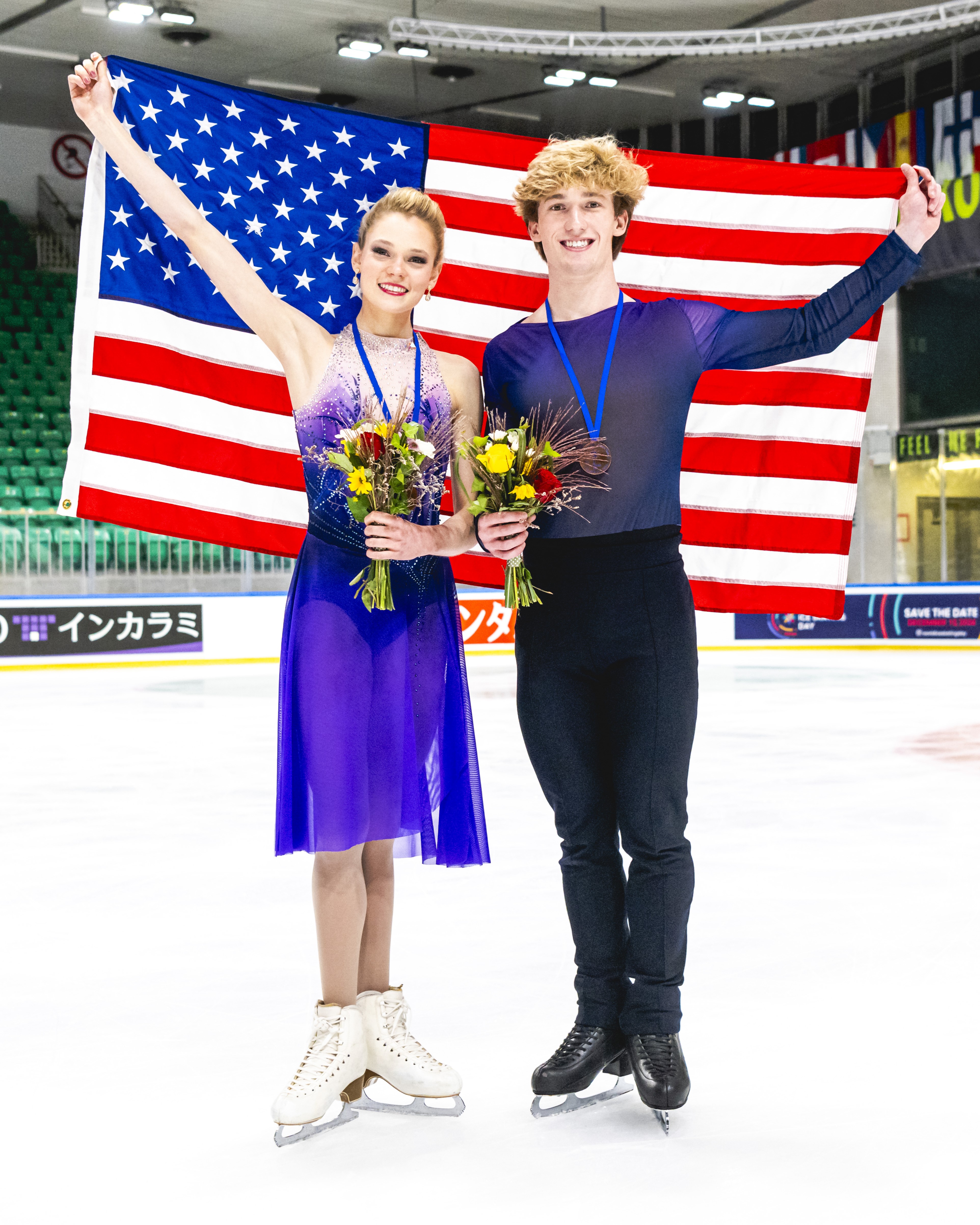 Caroline Mullen and Brendan Mullen pose holding a U.S. flag with their medals. Caroline is wearing a purple skating costume and Brendan is wearing a matching purple long sleeve shirt