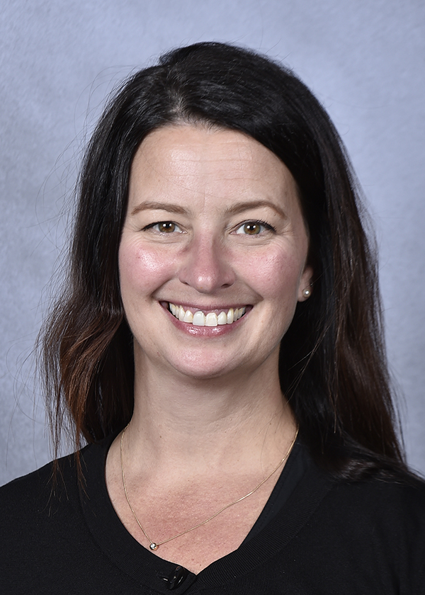 Headshot of Tracy smiling. She is Caucasian with long dark hair and is wearing a black shirt. 