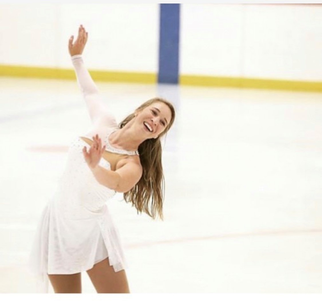 Sarah Fuller wears a white dress while skating and smiling up toward the sky. 