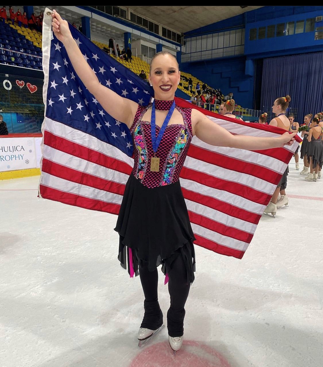Wearing a Skyliners free skate dress, Sarah Fuller holds up the American flag following the team's performance at the World Synchronized Skating Championships.