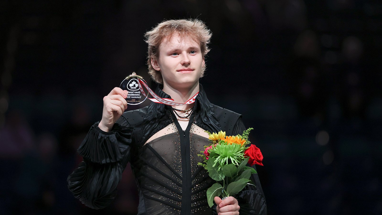 Ilia Malinin stands on top of the podium, holding a medal and flowers