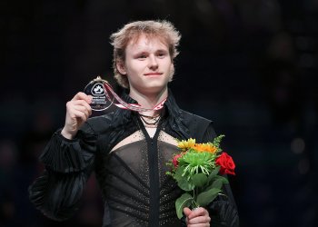 Ilia Malinin stands on top of the podium, holding a medal and flowers