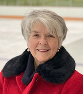 Headshot of Janet Champion. Janet is an older woman with white hair wearing a red winter coat with a black collar