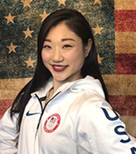 Headshot of Mirai Nagasu. Mirai is an Asian woman with long black hair wearing a white jacket with the Olympic emblem on the front and "USA" down the side